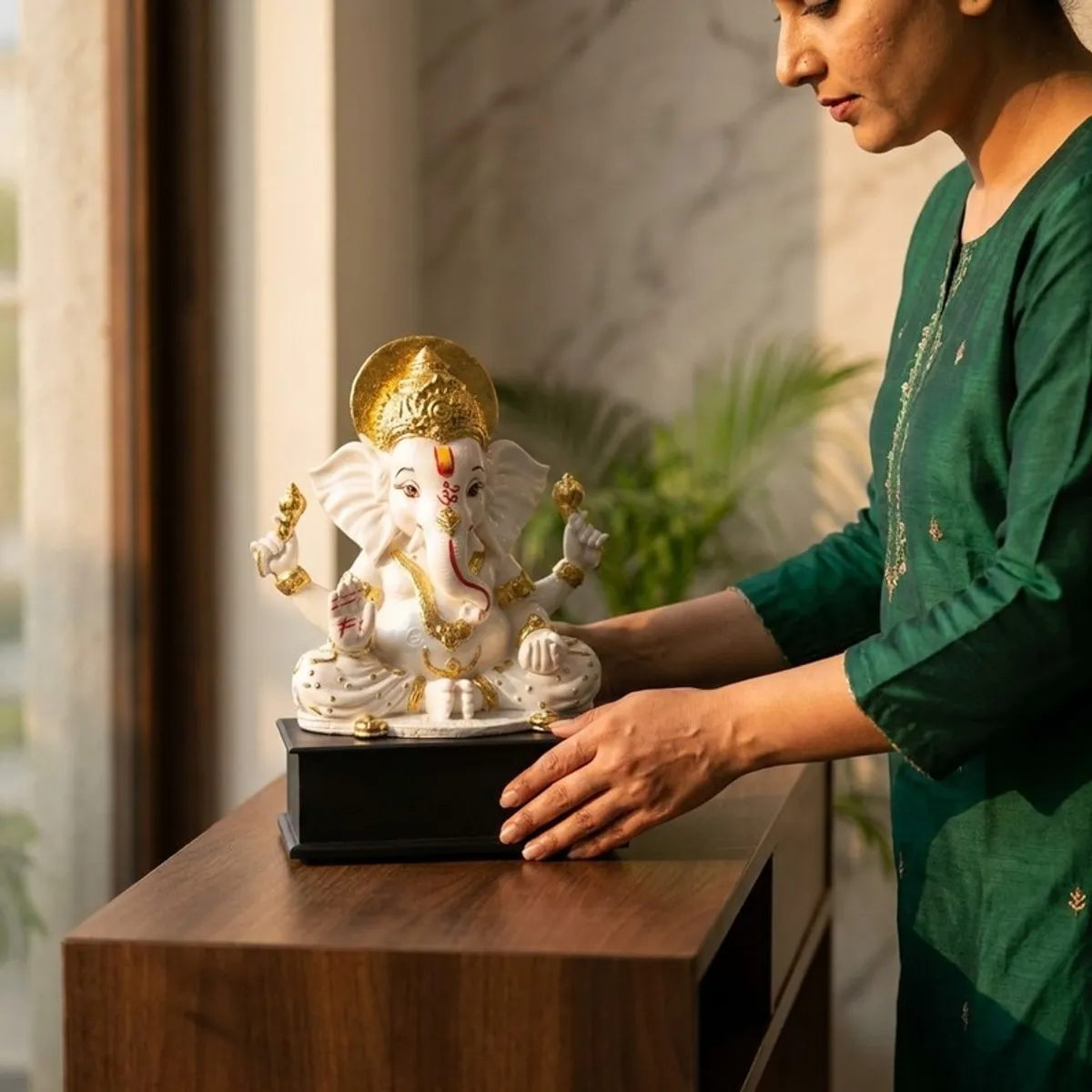 Person placing a white and gold Ganesha idol on a console table