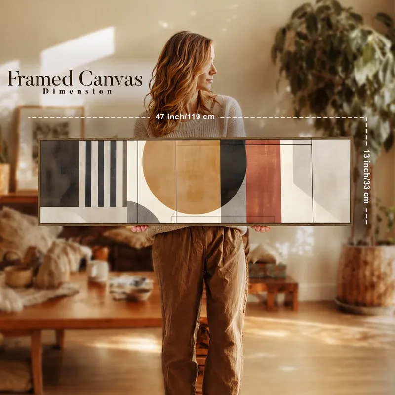 Person holding a long framed geometric canvas artwork in a warm-toned room