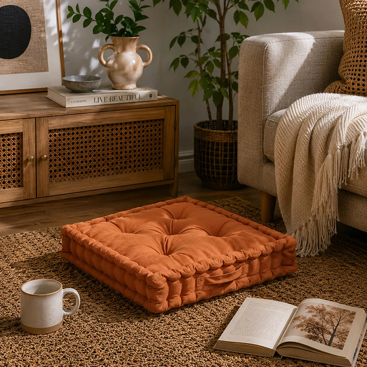 Tufted floor cushion placed on a textured rug in a warm living room beside a chair and open book.