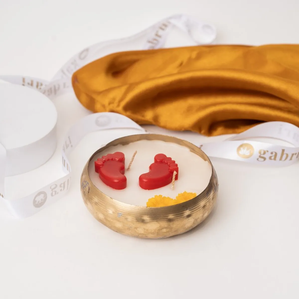 Round metal candle with white wax, red footsteps and yellow floral details on a white surface.