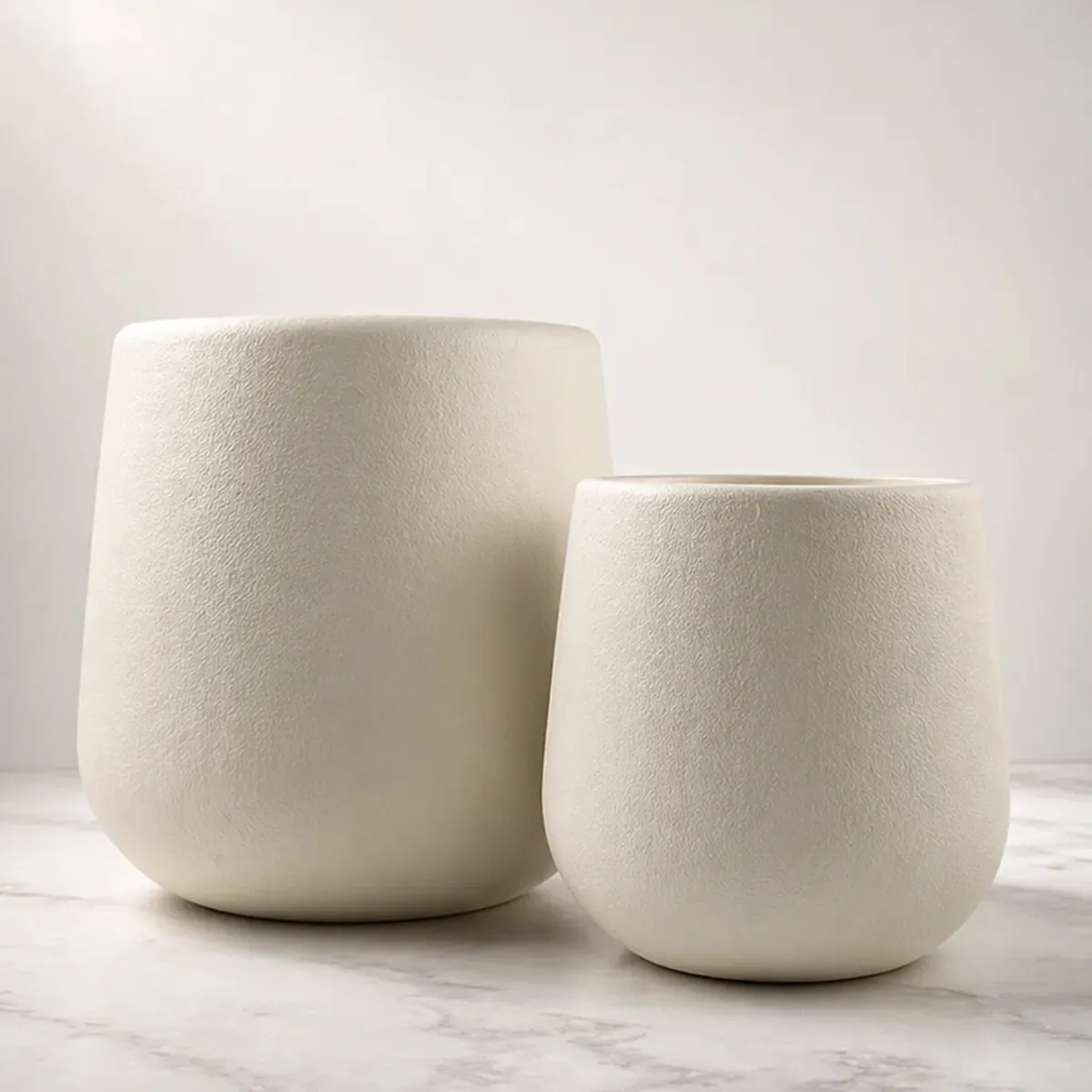 Two white matte cylindrical planters shown together on a light surface