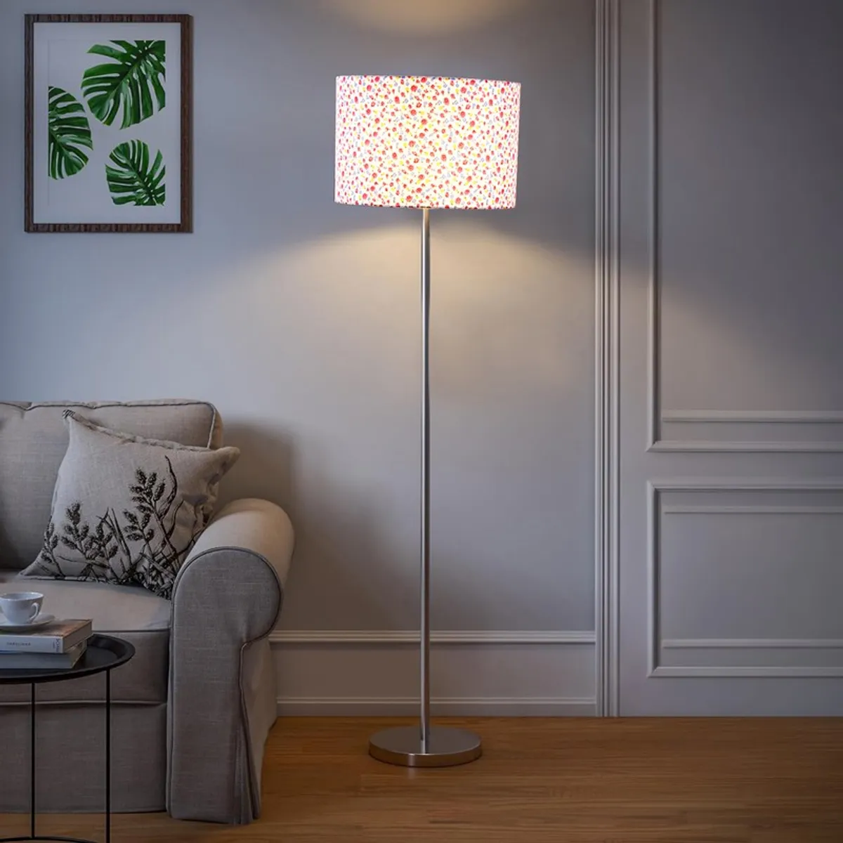 Lit multicolour floor lamp with steel base beside a grey sofa in a neutral room