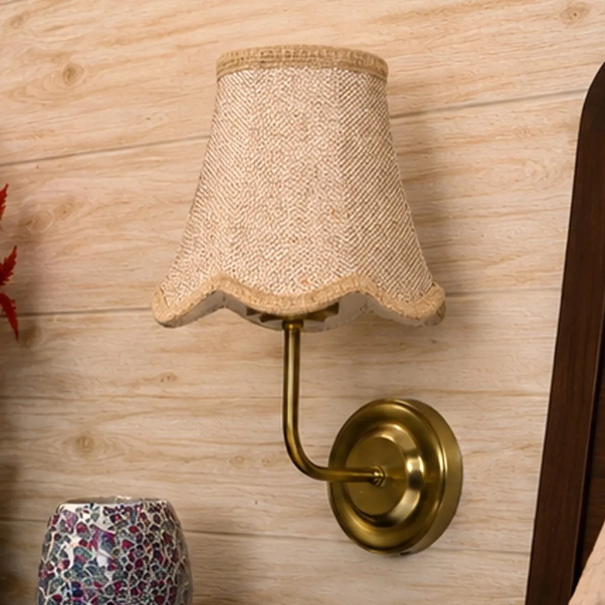 Beige shade and gold-toned wall lamp shown against a light wood wall