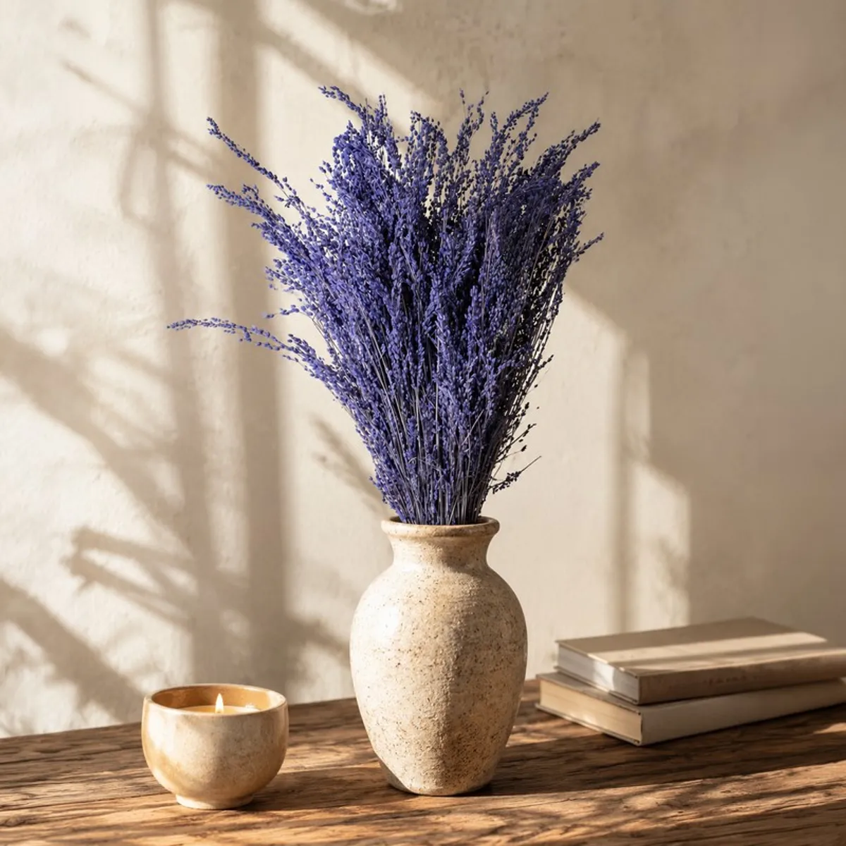 Purple dried flower bunch in a textured vase beside a candle and books