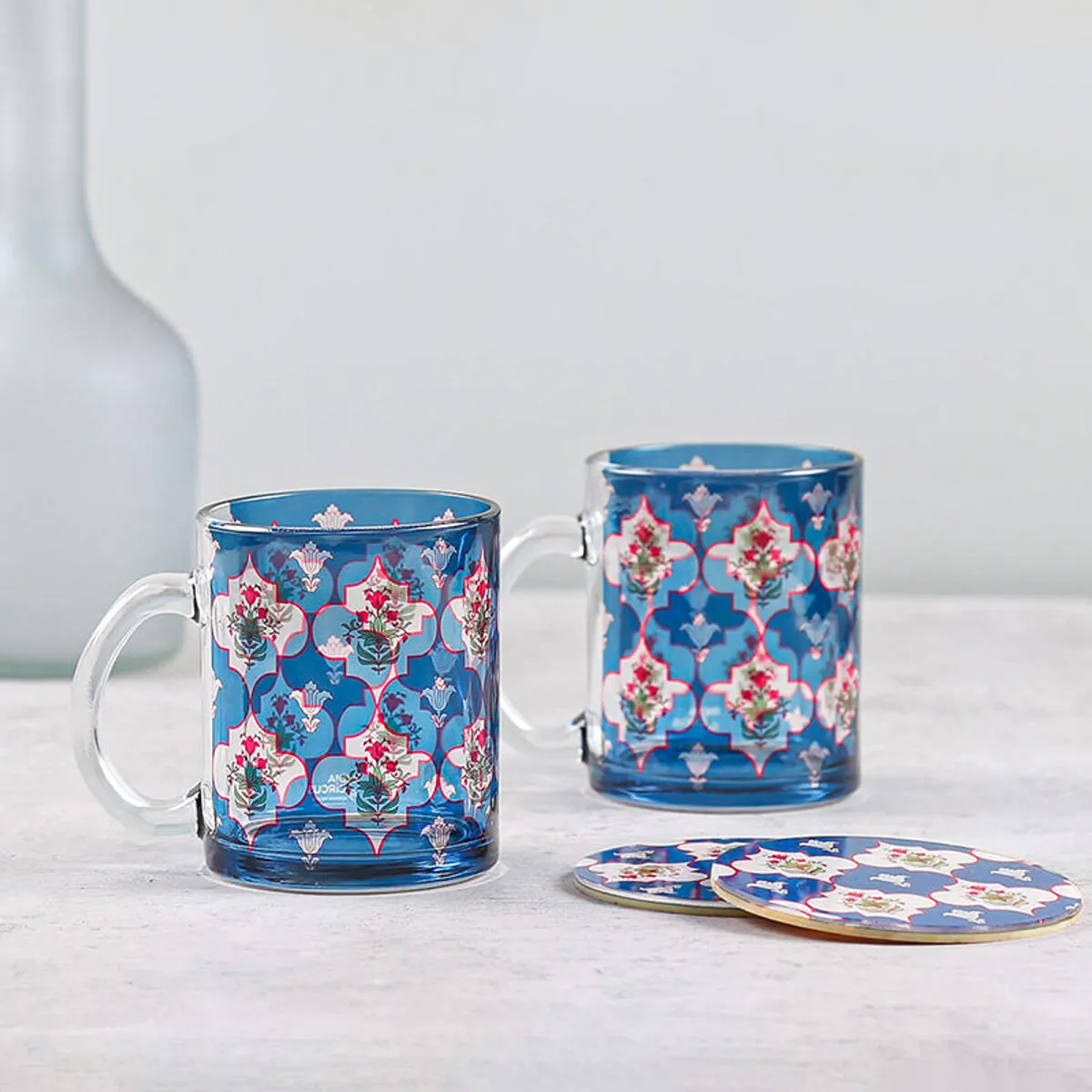 Two patterned blue glass mugs displayed with matching coasters